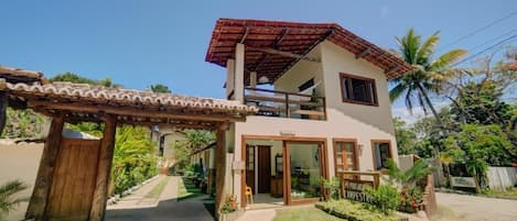 A two-story house with a wooden pergola entrance, a balcony, and a sign indicating a pousade camp.