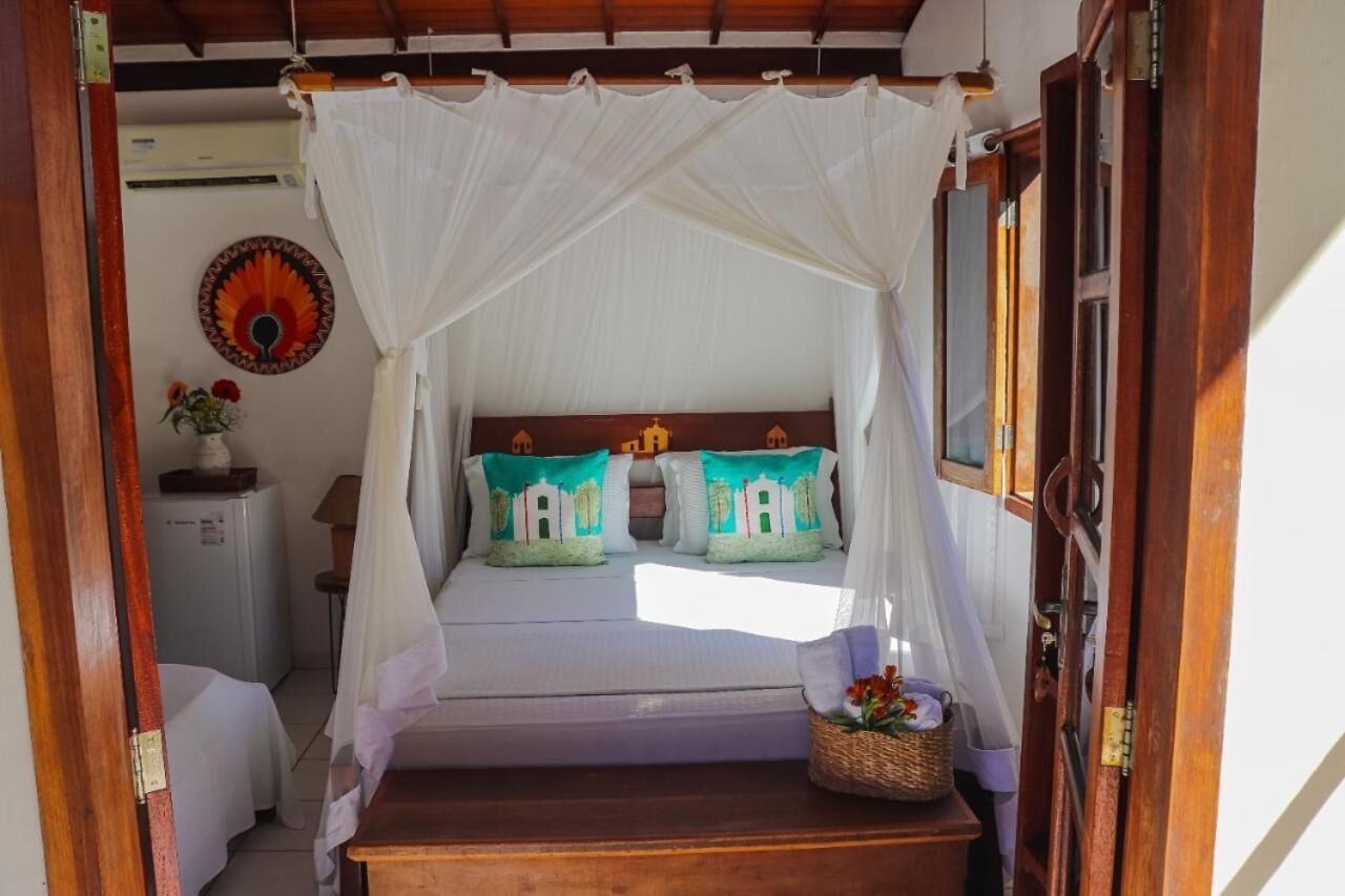 A bed with a canopy, a wall decoration, a small table with a basket, and a refrigerator.