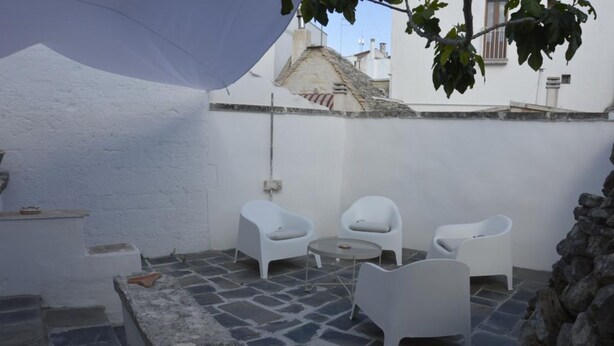 A small outdoor seating area with white plastic chairs and a round table, surrounded by stone flooring and white walls. - Oberdan Suites with Terrace (historical apartment in Alberobello) (Alberobello)