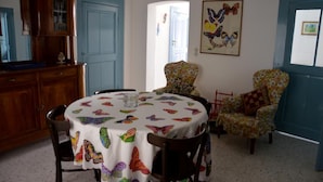 A dining area with a round table covered by a white tablecloth with colorful butterfly prints, surrounded by wooden chairs. There is a floral-patterned armchair and a red chair in the background. - Oberdan Suites with Terrace (historical apartment in Alberobello) (Alberobello)