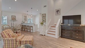 Ein geräumiges Wohnzimmer mit Sofa, Essbereich, Treppe und Fernseher.