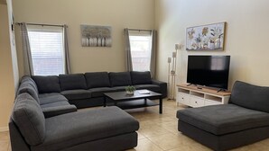 A modern living room with a sectional sofa, a coffee table, a TV on a stand, and artwork on the walls. - 5 Bedroom Pool Home (Davenport)