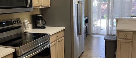 A modern kitchen with stainless steel appliances, wooden cabinets, and a tiled floor.