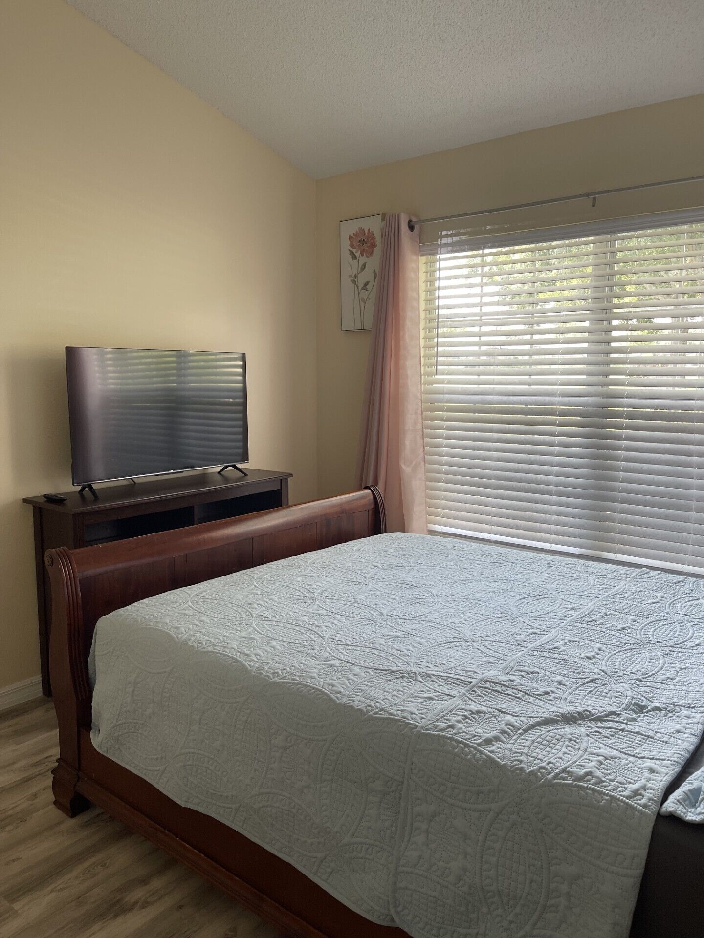 Quarto com cama, televisão sobre um suporte e janela com persianas.