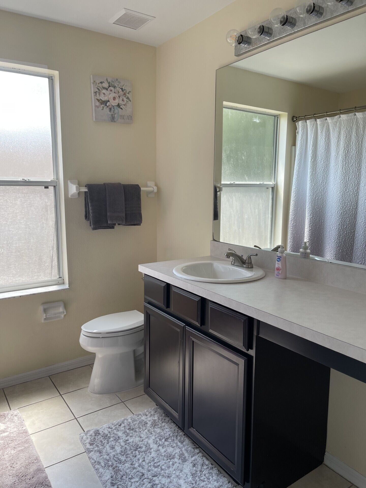 A bathroom with a toilet, sink, mirror, and a window.
