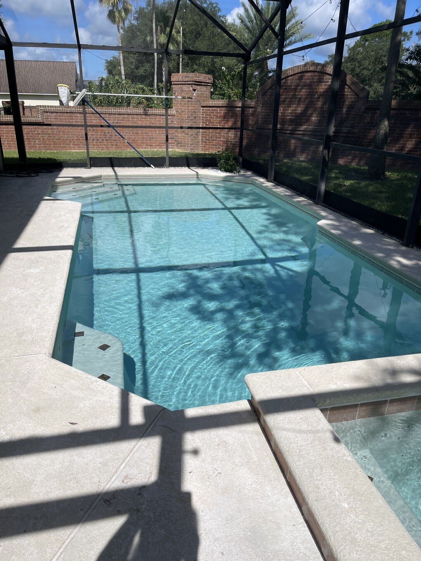 A rectangular swimming pool with clear blue water, surrounded by a brick wall and a metal fence.