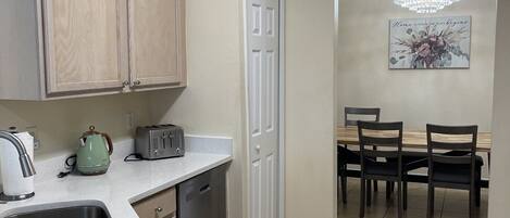 A kitchen with a countertop, sink, cabinets, a toaster, a kettle, and a dining area with chairs and a table.