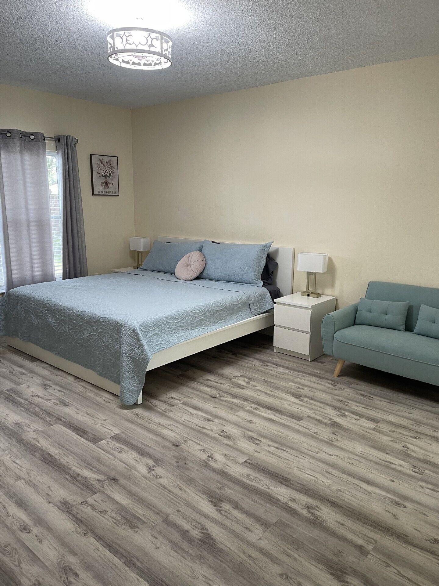 Une chambre à coucher comprenant un lit, des tables de chevet, une commode, un canapé et un luminaire au plafond.