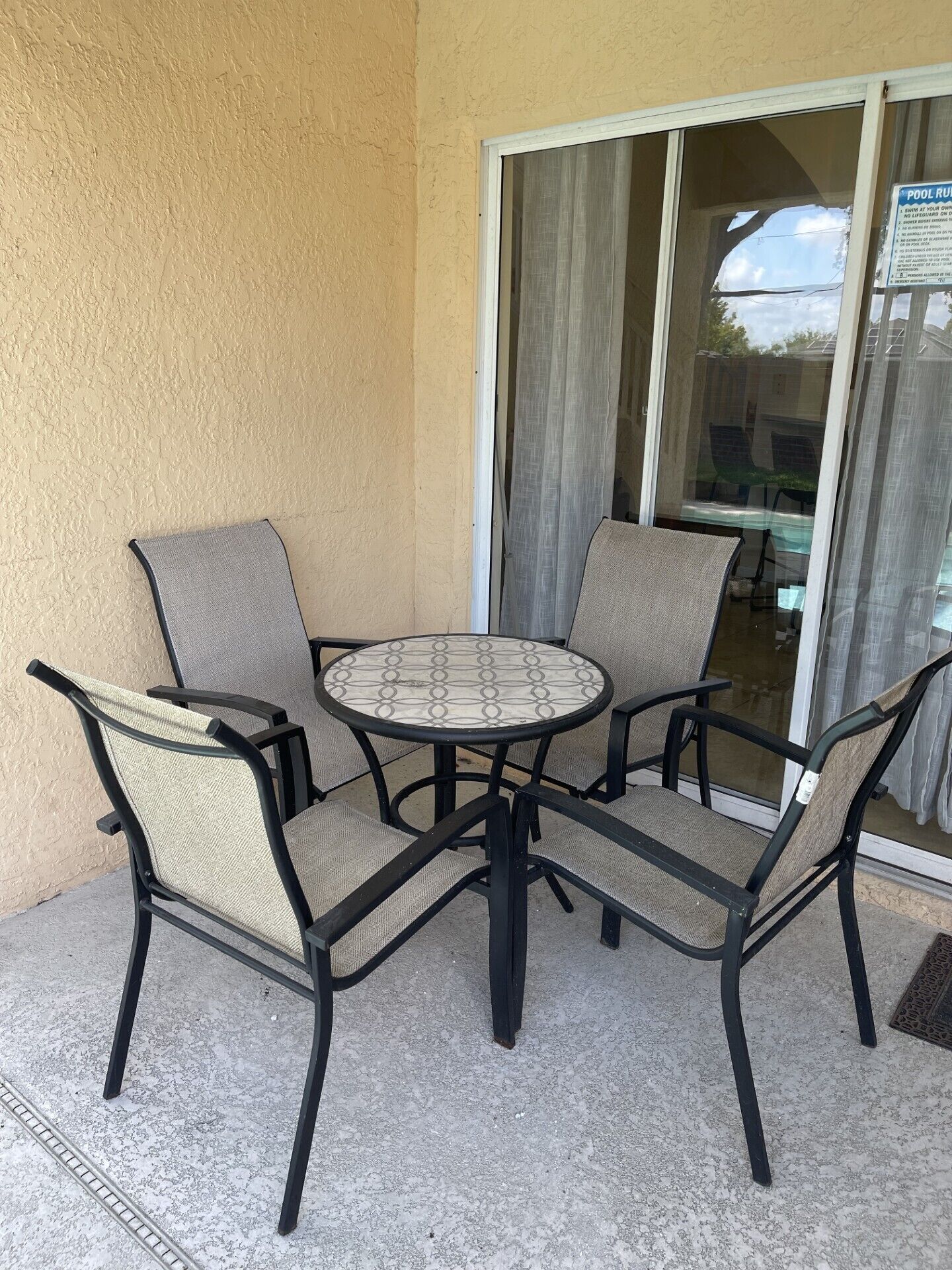 En patio med et rundt bord og fire stole, en skydedør i glas og en støbt gulv.
