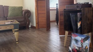 Ein Wohnzimmer mit Holzboden, einem braunen Ledersofa, einem kleinen Tisch und einem Bücherregal.