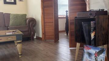 A living room with a wooden floor, a brown leather sofa, a small table, and a bookshelf.