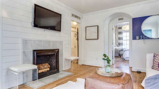 A modern living room with a fireplace, a mounted TV, and a hallway leading to a bedroom. - Heart Of The City ❤️ Hot tub, ITB, NC State Cameron Village  (Raleigh)