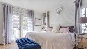 A bedroom with a large bed, a nightstand, a lamp, and a window with curtains. - Heart Of The City ❤️ Hot tub, ITB, NC State Cameron Village  (Raleigh)