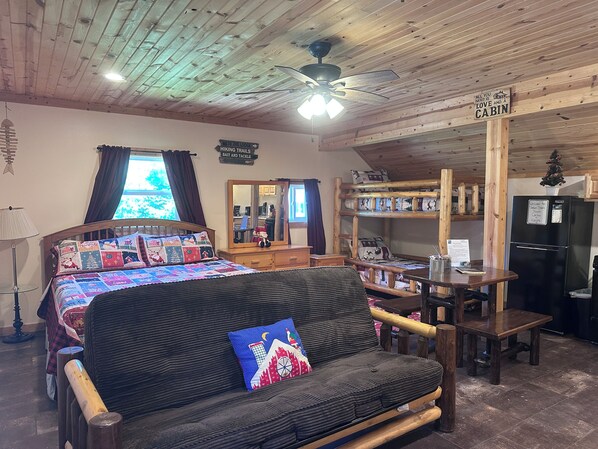 A cabin interior with a bunk bed, a sofa, a dining table, and a refrigerator. - Santa's Shack Studio - Near Pictured Rocks (Christmas)