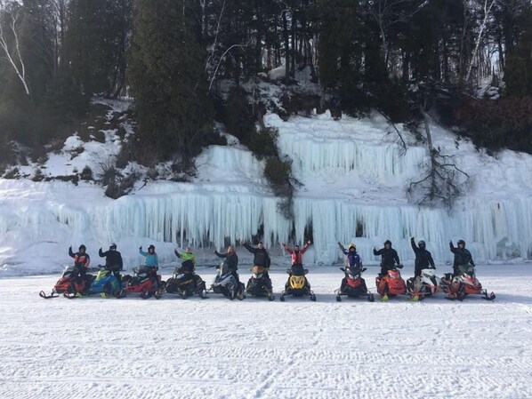 A group of people on snowmobiles in a snowy landscape with a frozen waterfall in the background. - Santa's Shack Studio - Near Pictured Rocks (Christmas)