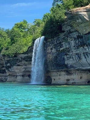 A waterfall cascading into clear turquoise water, surrounded by rocky cliffs and lush greenery. - Santa's Shack Studio - Near Pictured Rocks (Christmas)