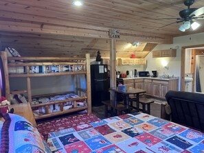 A cabin interior with bunk beds, a kitchen area, and a dining table. - Santa's Shack Studio - Near Pictured Rocks (Christmas)