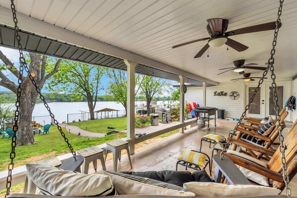 A covered porch with outdoor seating, a view of a lake, and a patio area with tables and chairs.
