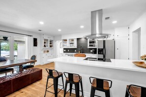 A modern kitchen with white cabinetry, a central island, and a dining area with a bench and bar stools.