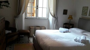 Une chambre d’hôtel bien rangée, avec un lit, un banc, une valise et une lampe.