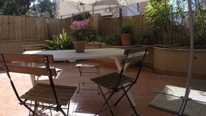 Une terrasse extérieure avec une table et des chaises, un grand parasol et des plantes en pot.