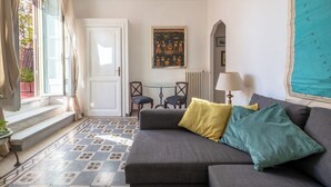 Un salon confortable avec un canapé, une petite table et des chaises. Il y a un tableau au mur et une fenêtre avec des rideaux.