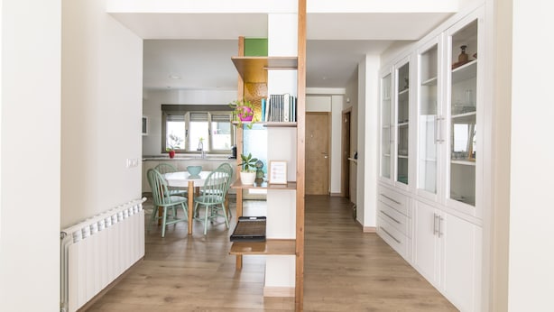 Una cocina moderna con armarios blancos, piso de madera y un comedor con mesa y sillas.