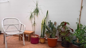 Un patio con una silla de metal, una mesita de madera y diversas macetas con plantas.
