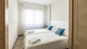 Una habitación de hotel con dos camas, una puerta de madera y una ventana con cortinas traslúcidas.