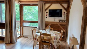 A dining area with a wooden table set for four, a television mounted on the wall, and a view of greenery outside. - Beautiful apartment for 4 guests with WIFI, TV and balcony (Saint-gervais-les-bains)