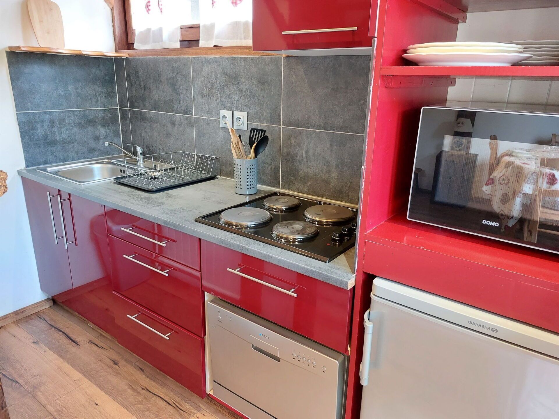 A modern kitchen with red cabinets, a stainless steel stove, a dishwasher, and a microwave.