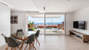 A modern living room with a glass dining table, four chairs, a flat-screen TV, and a view of the sea through large sliding doors. - Premium villa with private pool and sea views (Ancla Mar nº4) (Roses)