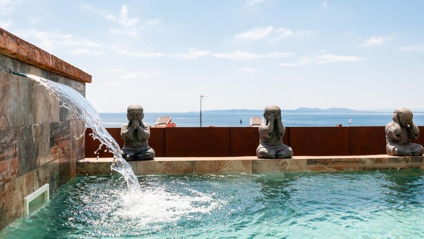 A pool with water flowing from a wall, stone statues, and a view of the sea. - Premium villa with private pool and sea views (Ancla Mar nº4) (Roses)
