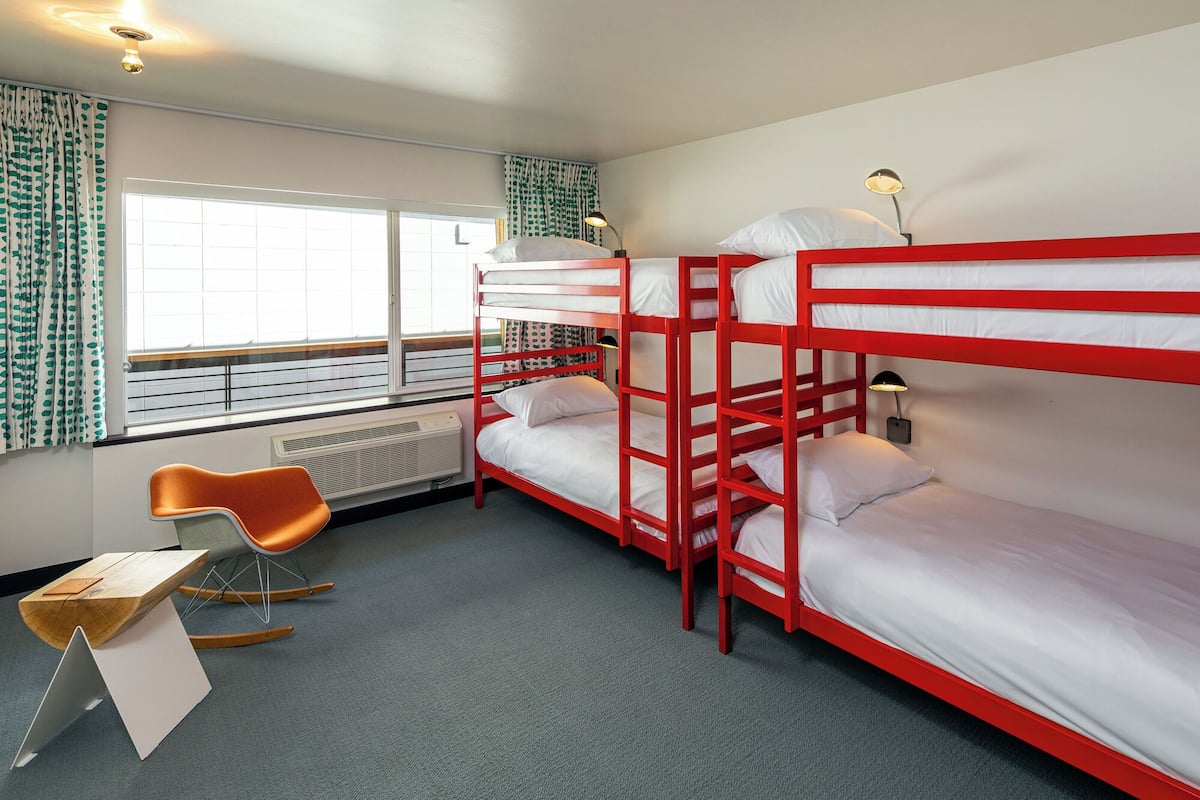 A bunk bed room with a window, a radiator, a chair, and a desk.