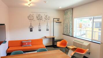 Una habitación moderna con un sofá naranja, dos mecedoras, una mesa de madera y un amplio ventanal con cortinas.