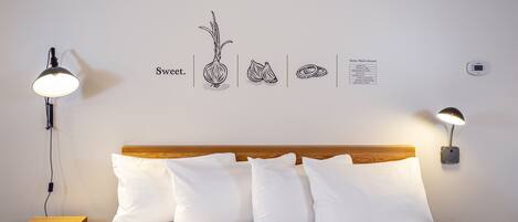 A neatly made bed with white bedding and multiple pillows, a wooden headboard, and two wall-mounted lamps.