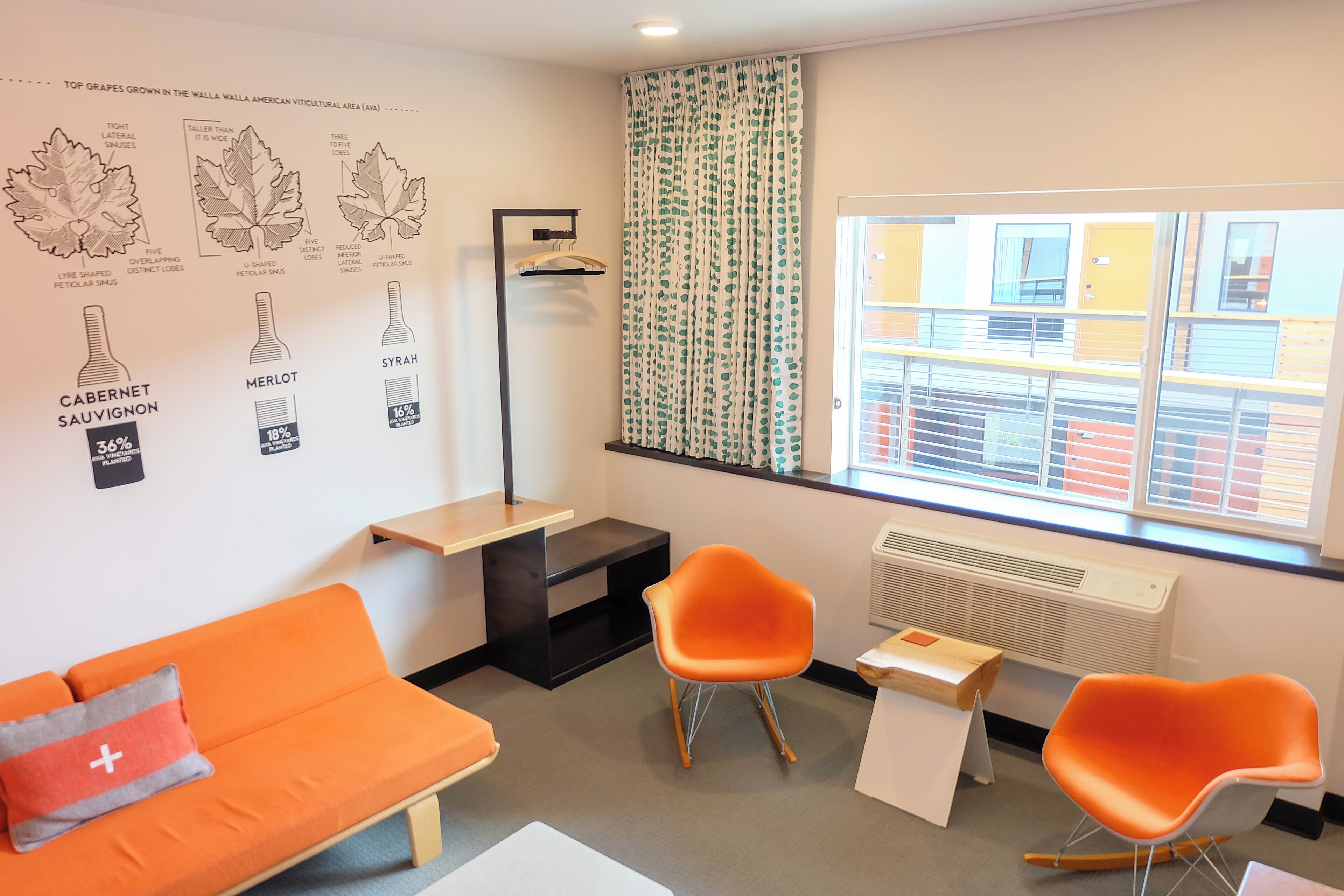 A modern room with an orange sofa, two orange chairs, a small table, and a window with a view of buildings.