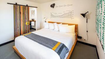 Una habitación de hotel con una cama grande, cabecero de madera, un mapa en la pared, un escritorio con silla, y un baño con perchero.