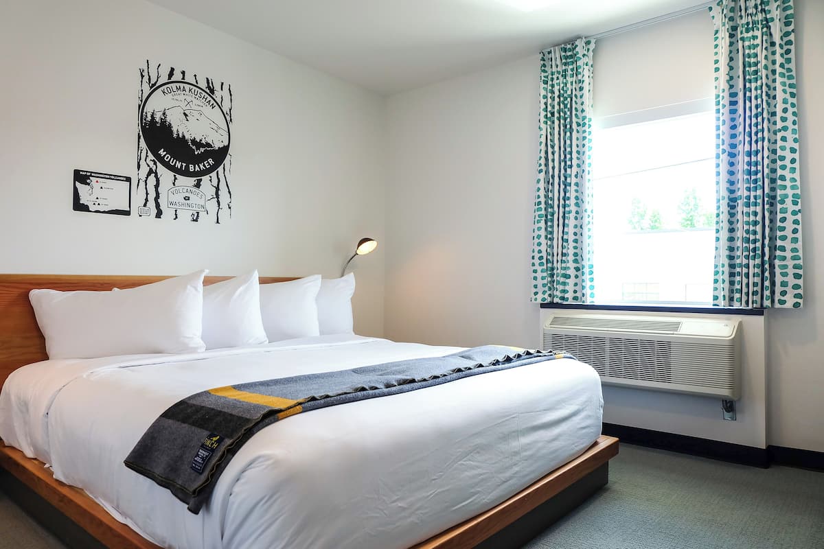 A neatly made bed with white linens, a blue and yellow blanket, and a wall-mounted lamp.