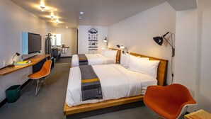 Habitación de hotel con dos camas, un escritorio con computadora, una silla y un televisor.