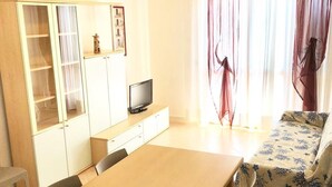 A compact room with a wooden table, chairs, a TV, a bed with patterned bedding, and a wardrobe with glass doors.