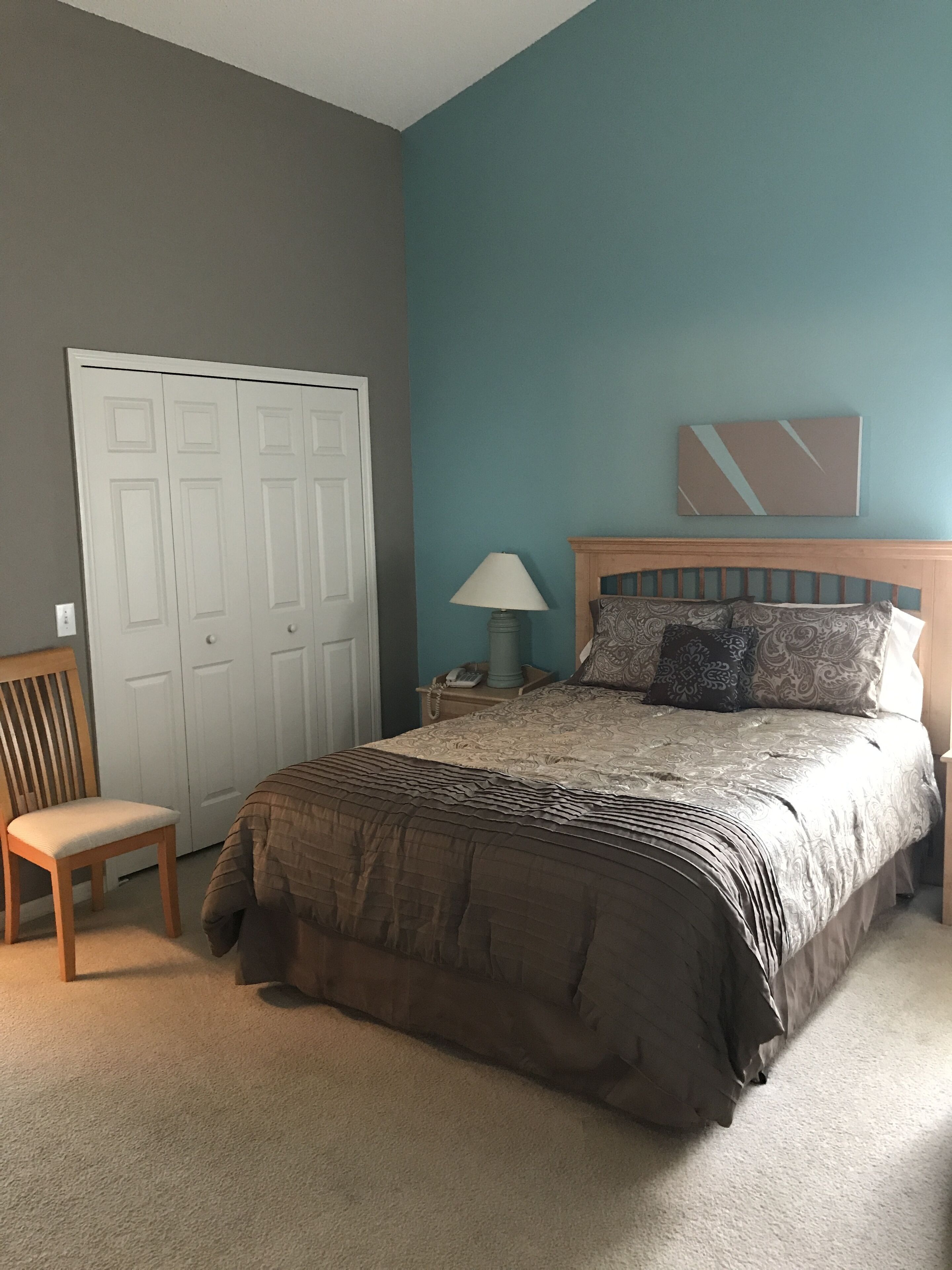 Ein Schlafzimmer mit einem Bett, einem Sessel, einem Kleiderschrank und einem Nachttisch mit Lampe.