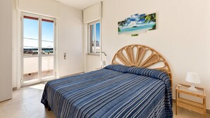 Un dormitorio con cama, mesita de noche, un cuadro y puerta corrediza de vidrio que da a un balcón.