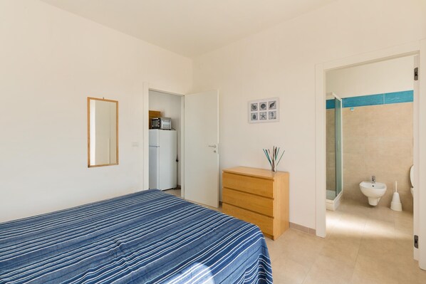 Un dormitorio con cama, cómoda de madera, espejo y baño con ducha e inodoro.