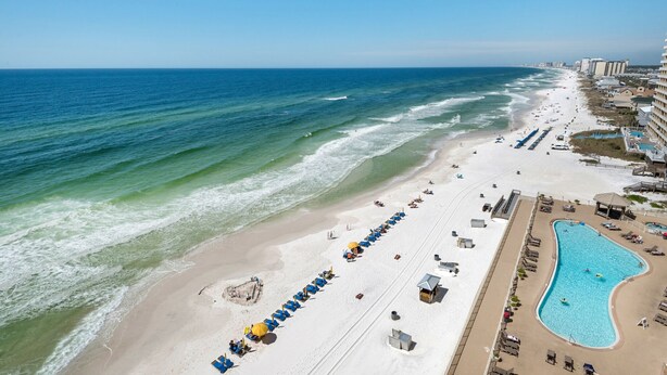 A beach resort with a long row of beach chairs and umbrellas, a swimming pool, and a view of the ocean. - Treasure Island 1003 (Panama City Beach)