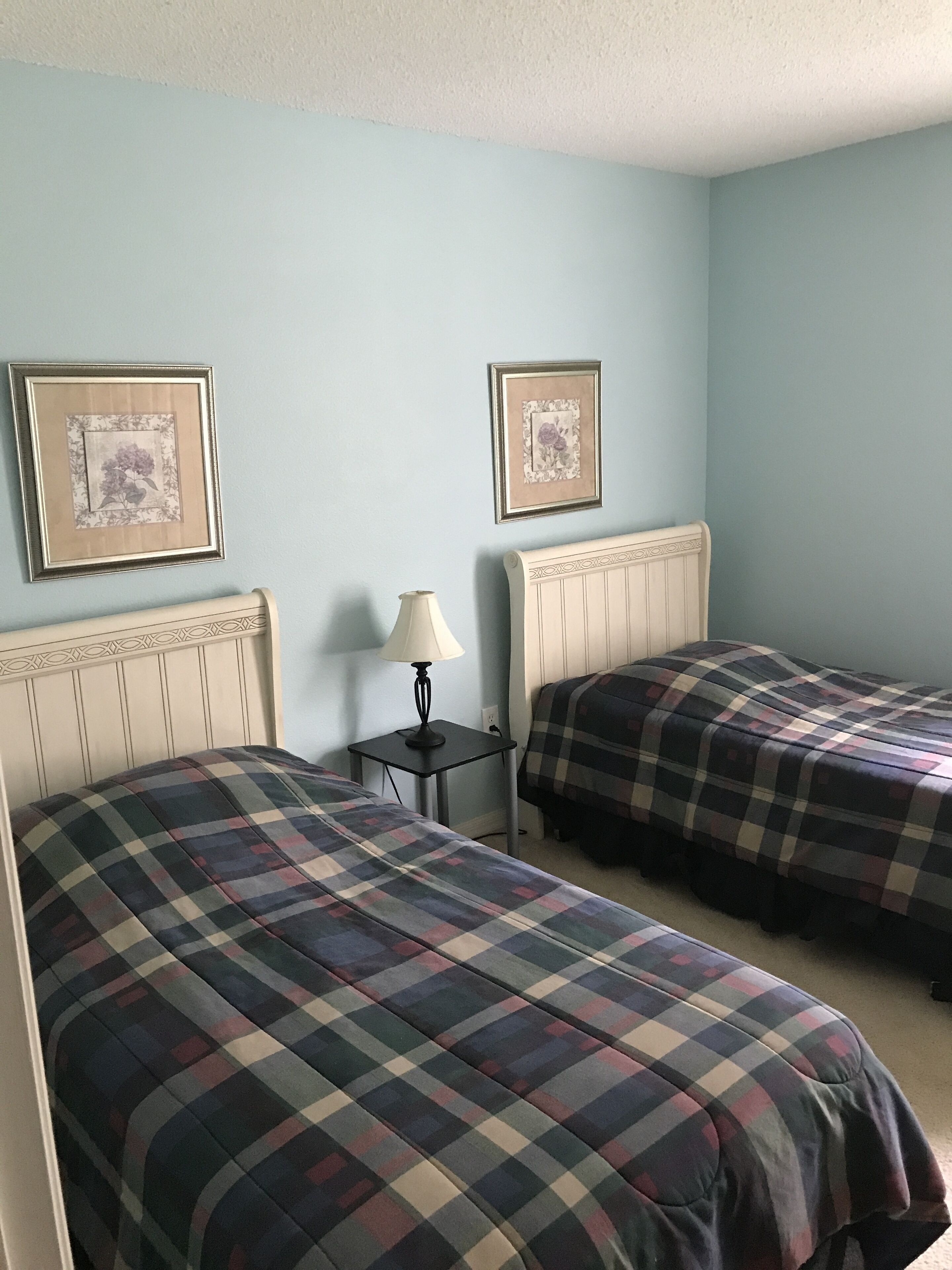 Une chambre avec deux lits, une table de chevet et deux tableaux encadrés accrochés au mur.