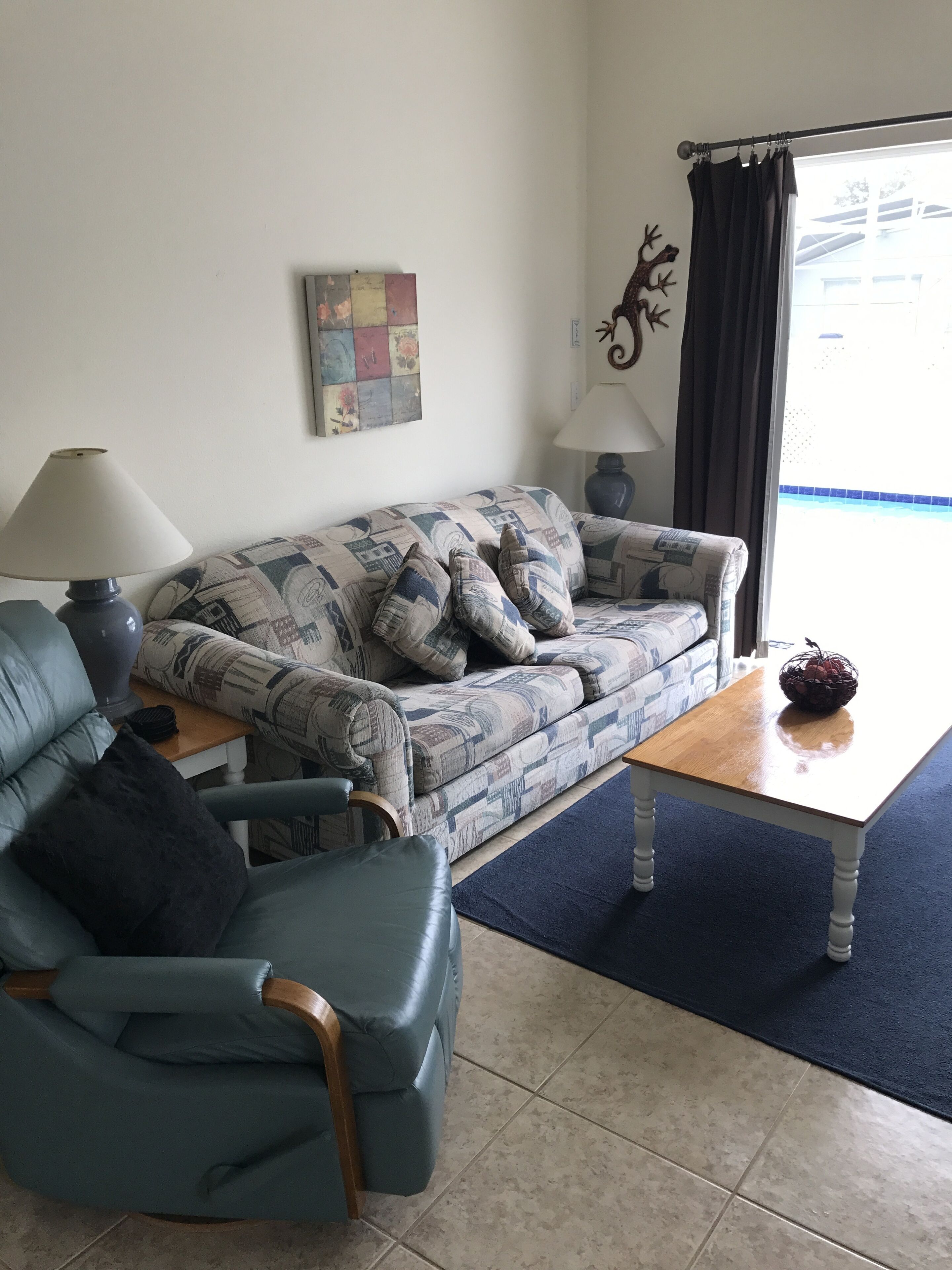 A living room with a patterned sofa, a blue armchair, a wooden coffee table, and a lamp.