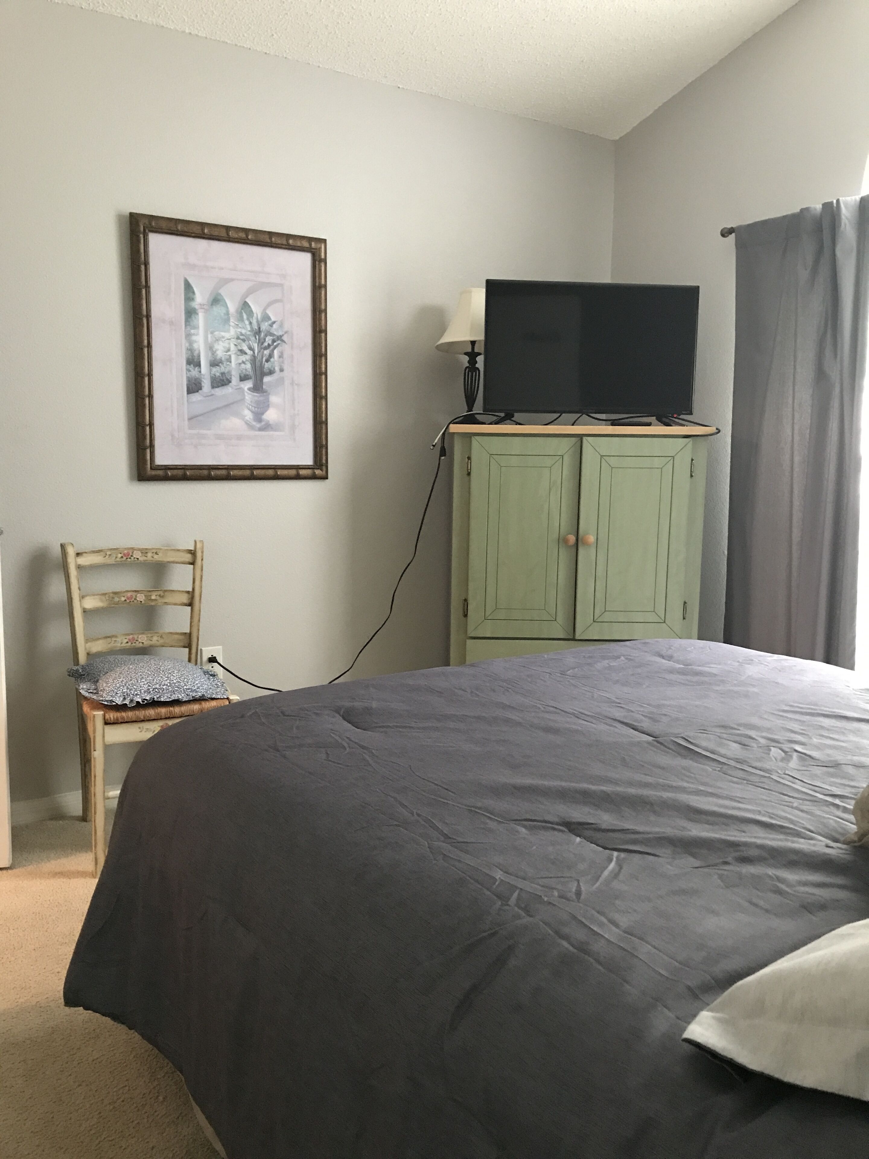 Een slaapkamer met een bed, een televisie op een kast, een stoel en een lijst met een foto aan de muur.
