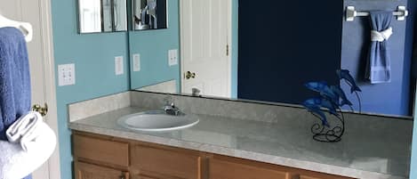 Un baño con lavamanos, armarios de madera, un espejo con iluminación, un perchero para toallas y una alfombra azul.