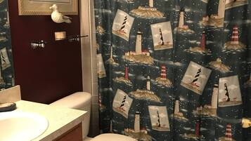 A bathroom with a toilet, a sink, a mirror, and a shower curtain with a lighthouse pattern.